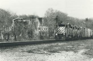 A freight train passes houses on the south side of the track