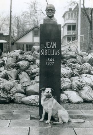 A neighborhood dog and a bust of composer Jean Sibelius mournfully guard heaped-up garbage in a park at Kendal Ave