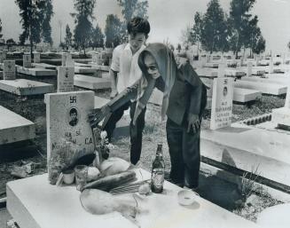 Relatives place offerings of food and drink on a grave in the national military cemetery at Bien Hoa, South Viet Nam, where headstones are marked with(...)