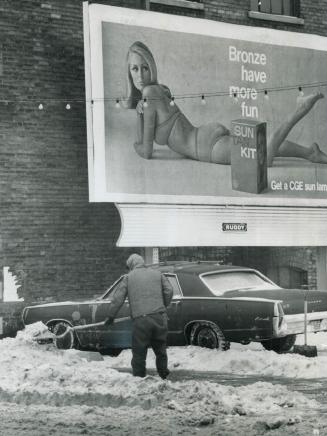 Bikini-Clad beauty, obviously impervious to the cold, looks on as a parking lot attendant begins the job of removing some of the 11 inches of snow Tor(...)