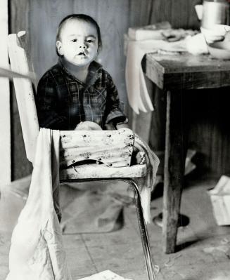 Baby Marilyn, 1 1/2, stares from her chair in the kitchen of a cold, untidy shack on the reserve