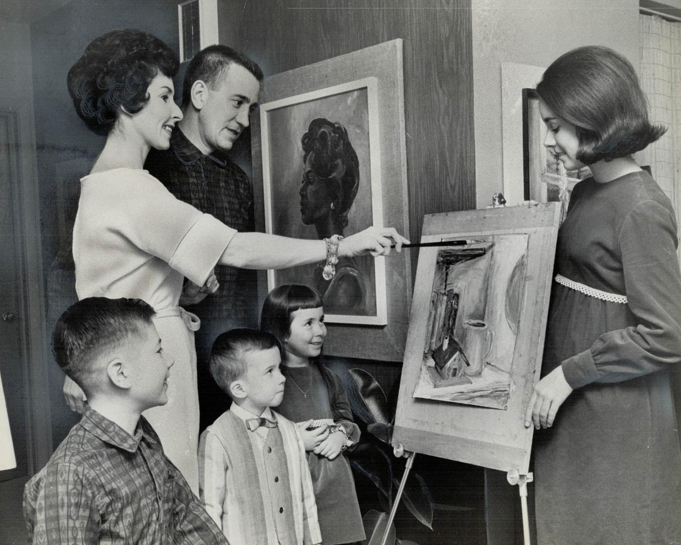 The Mills Family, wearing some of mother's handiwork, admires painting she's preparing for February show
