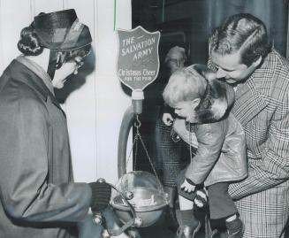 L. A. Ward holds up his 2-year-old son, Richard, so he can put a donation into the Salvation Army kettle on Queen St. tended by Glennyth Necho, 21, of(...)
