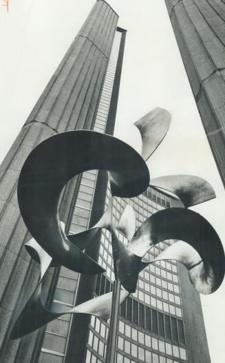 An abstract metallic sculpture, with the curved towers of the Toronto City Hall in the backgrou ...