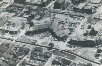 Aerial view of construction site on parcel of land between two roadways, with houses and low-ri ...