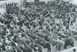 Overhead view of room full of people seated in church pews.