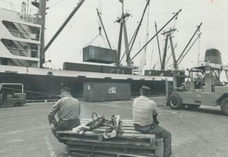 Image shows deck workers sitting with the cargo ship in the background.