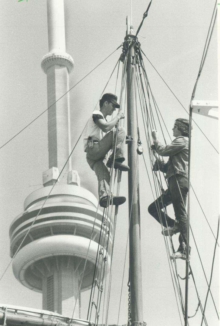 Image shows two people climbing up the mast with a CN Tower in the background.
