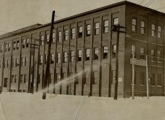 Exterior view of three-story brick building with several windows propped open by chairs. Sign o…