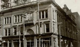Façade of three-storey stone building visible from mid-level of ground floor up. Sign above str…