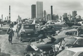 Image shows an auto-wrecker's yard with Toronto skyscrapers in the background.