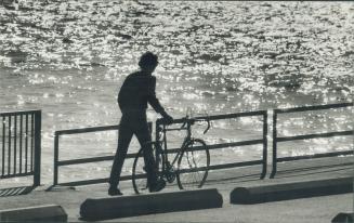 Image shows a cyclist walking a bike along the Harbour with a lake in the background.