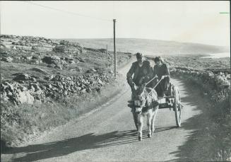 Their day's work done, a young Irish lad and his father head home by donkey cart along the winding coastal road of County Clare which borders the waters of Galway Bay