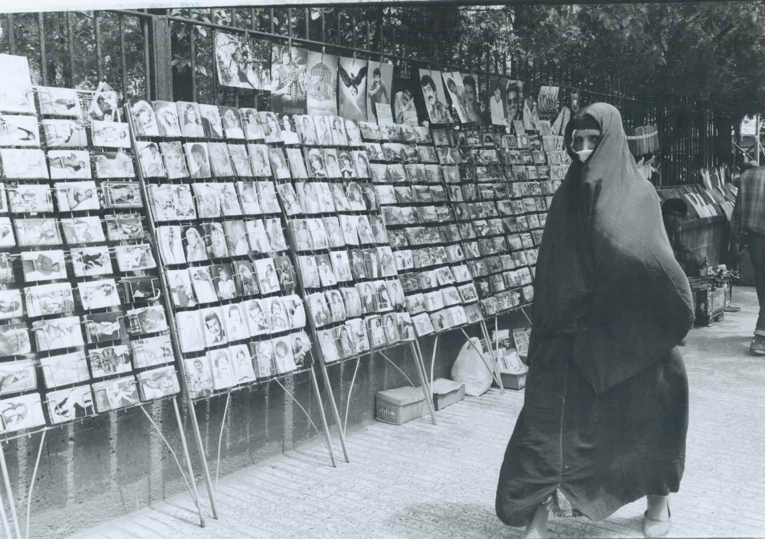 Velled woman walks by displays of pop star photos