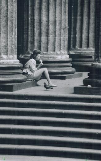On cathedral steps in Kazanski Square, a young woman office worker sits by classical columns to eat an ice-cream cone