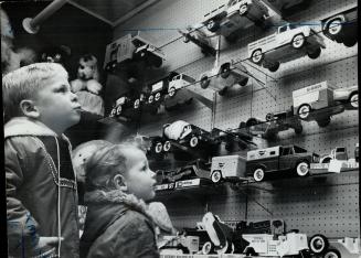 Looks of longing fill the faces of these two children as they admire an array of toy cars and trucks on a store shelf