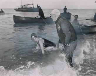 At completion of channel swim near Dover, England, coach Gus Ryder is shown wading into water as Marilyn comes ashore on hands and knees. She was 17 w(...)