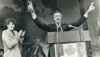 Triumphant Joe Clark displays a wide grin and a double victory sign as his wife, Maureen, applauds