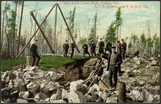 Colorized photograph of a group of men with mining machinery standing on rocks.