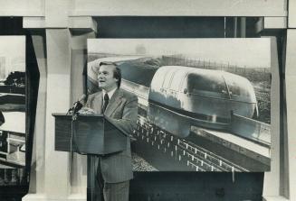 Premier Davis stands before picture of prototype of magnetic cushion train