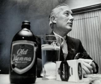 A bottle of Beer and a package of cigarettes firmly in his grasp, John Devlin smiles his satisfaction at thwarting a takeover bid for Canadian Breweri(...)