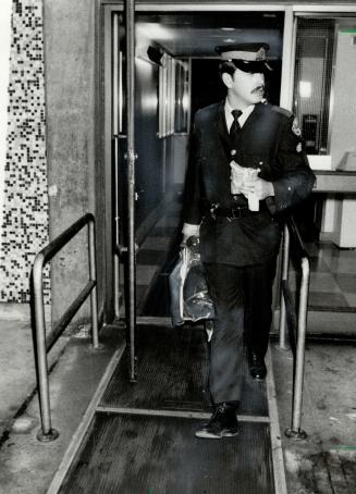Constable's clothes: A policeman carries the uniform and other articles worn by the wounded Constable Glen Bacon from Wellesley Hospital