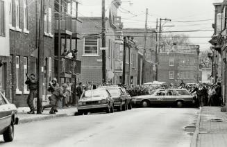 Street drama: Curious spectators watch as heavily armed police wait out a gun-wielding man who took over his parents' house yesterday