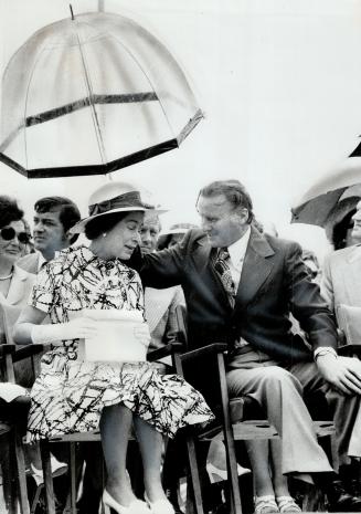 W. Chester MacDonald, Co-chairman of the Prince Edward Island summer games, holds a transparent umbrella over the Queen during a brief shower yesterda(...)