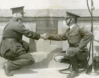 Sergeant R. Cox (left), representing Canada, and Lieut. Oscar Haffa, representing the United States, clasp hands at the international border on new Peace Bridge between Fort Erie and Buffalo