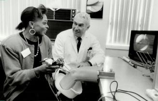 Learning tool, Sprinter Angela Balley inserts arthroscope into a mock-up of a knee and views image on a television monitor as Dr. Robert Jackson looks(...)