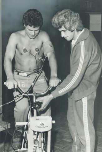 Plugged into heart-testing machine, defenceman Jim McKenny rides bicycle during physical fitness tests for Leafs at the Gardens. Zoran Linzender of Ad(...)