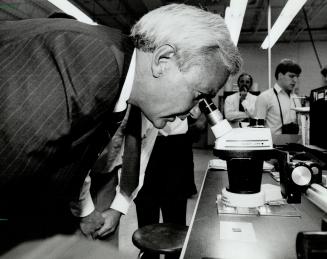 Eyeing the future, Premier David Peterson helps illustrate a campaign pitch for more high-tech by peering at a microchip during a Kitchener factory visit yesterday