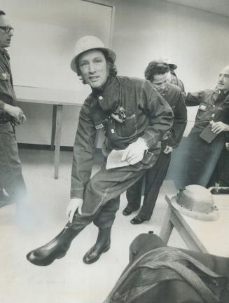 Doing a balancing act, Prime Minister Pierre Trudeau zips up rubber boots as he outfits himself for underground tour at Falconbridge Nickel Mines near(...)