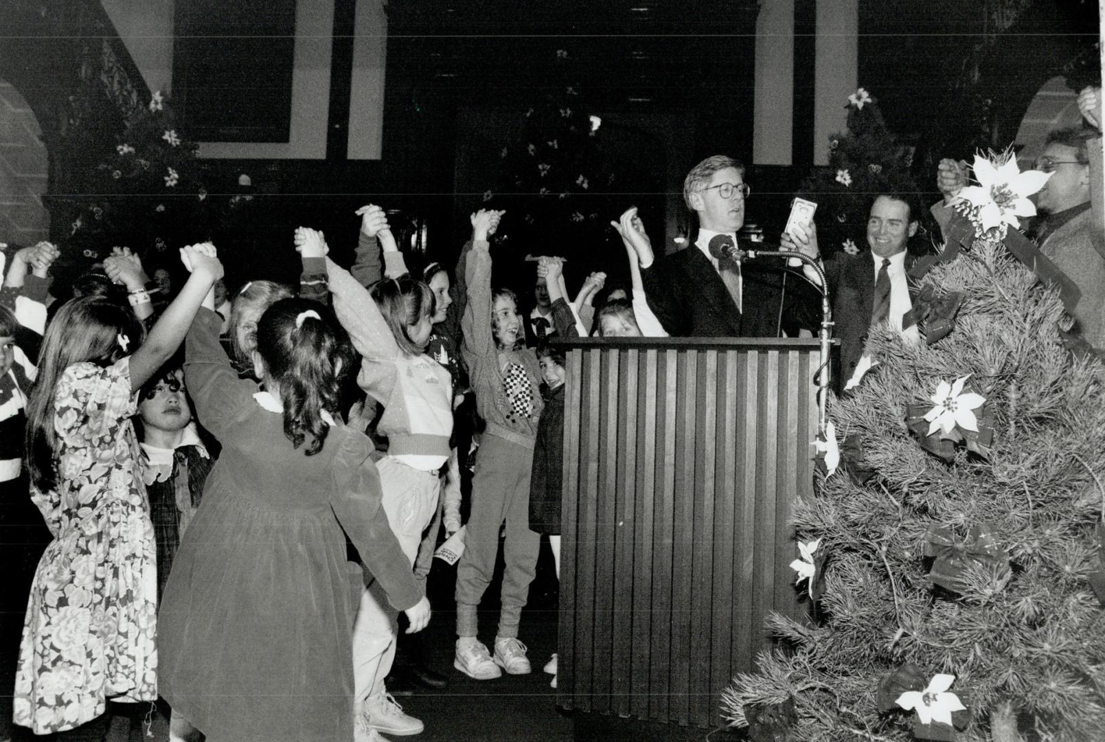 Rae puts in plug for holidays. Premier Bob Rae invites children in the Legislature lobby to join hands yesterday for the Lights Across Canada ceremony(...)