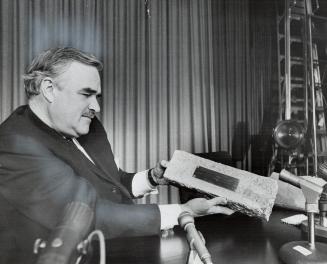So, London bridge fell down . . . Ontario Premier John Robarts sits looking dubiously at a 17-pound brick that used to be part of famed London Bridge.(...)
