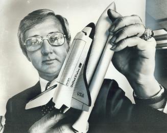 John Latin holds model of Space Shuttle, 1st re-usuable spacecraft
