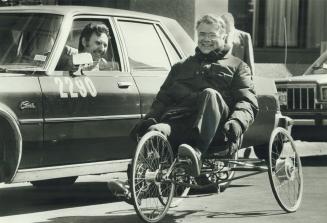 Happy journey: Robert Perkins, aboard the pedal-powered mansized vehicle he invented, gets an affectionate smile from a cab driver on a Toronto street