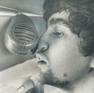 Using his nose to operate radio microphone garage mechanic John Radmacher shows how he called for help after two men tied him hand and foot during robbery at taxi garage on George St