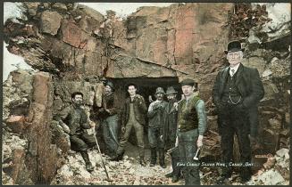 Several miners and a mine executive standing in front of an opening to a mine.