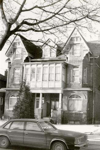 A three-storey duplex with a glassed-in balcony on the second floor between the two houses, sup…