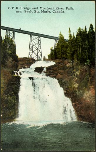 A waterfall in the foreground, with a bridge passing overhead.