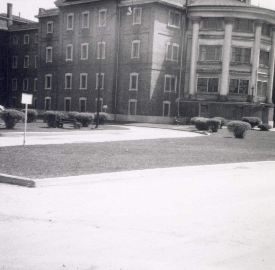 Shows a large brick four-storey building, with a rounded section ornamented by colonnades on th ...