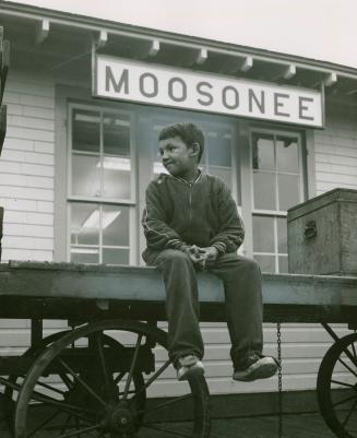 Boy sits on rail outside Moosonee train station