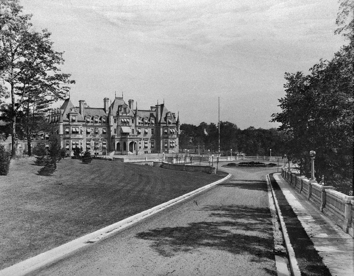 Image shows a road view with a multi storey house in the background.