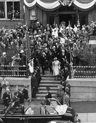 Image shows a lot of people around the stairs where the royals are going down to the automobile ...