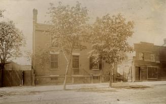 A sepia-toned photo of a 19th-century brick building with two tall trees in front. 