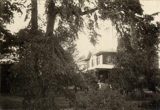 Image shows a limited view of a two storey house. There are a number of trees in front of it.