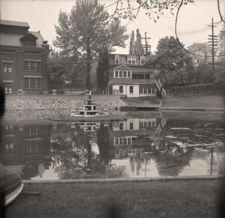 Image shows a water pond with a few houses in the background.