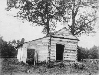 Image shows a log cabin. There are a few trees behind it.