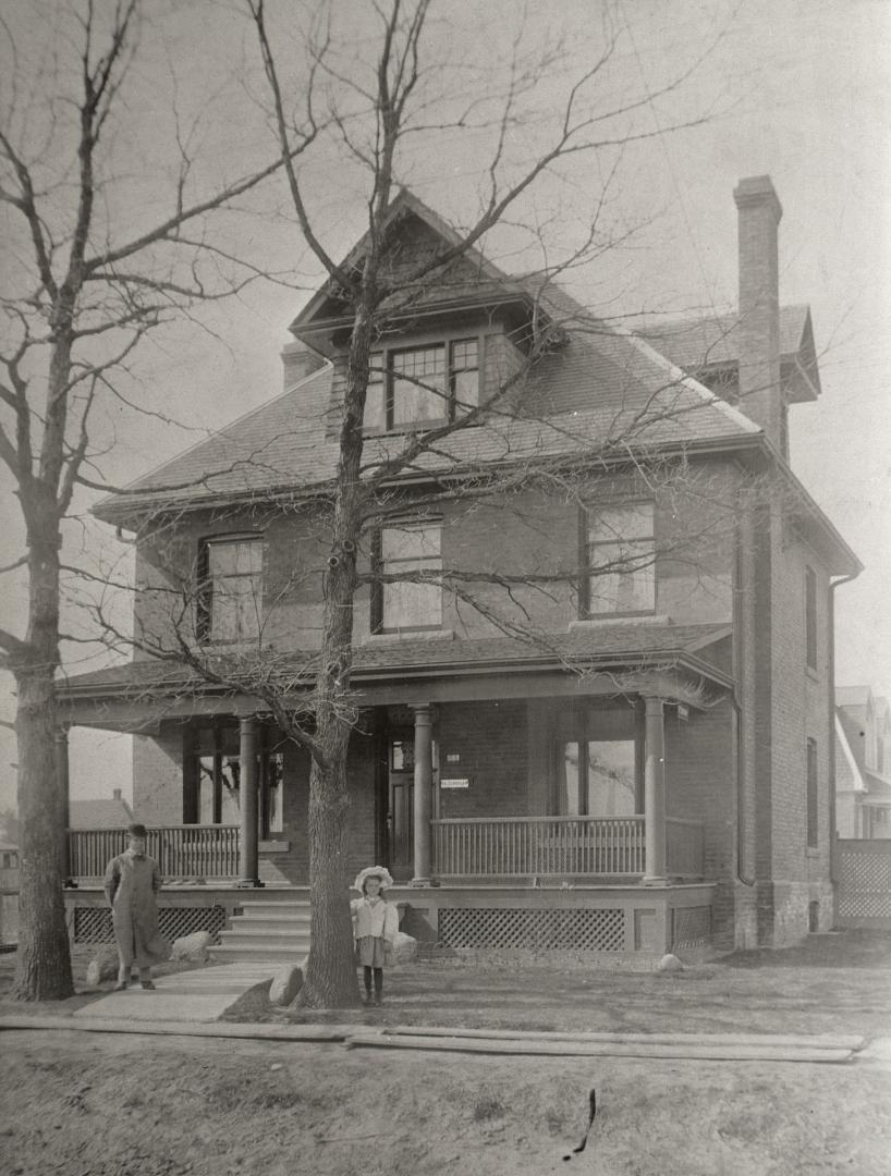 Image shows a three storey residential house with a few trees in front of it.